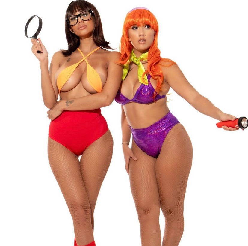 Two models wearing costume sets designed to resemble the characters Daphne and Velma from the movie 'Scooby Doo'. One model is wearing a red top and high waisted shorts, and the other is wearing a purple top and high waisted shorts.