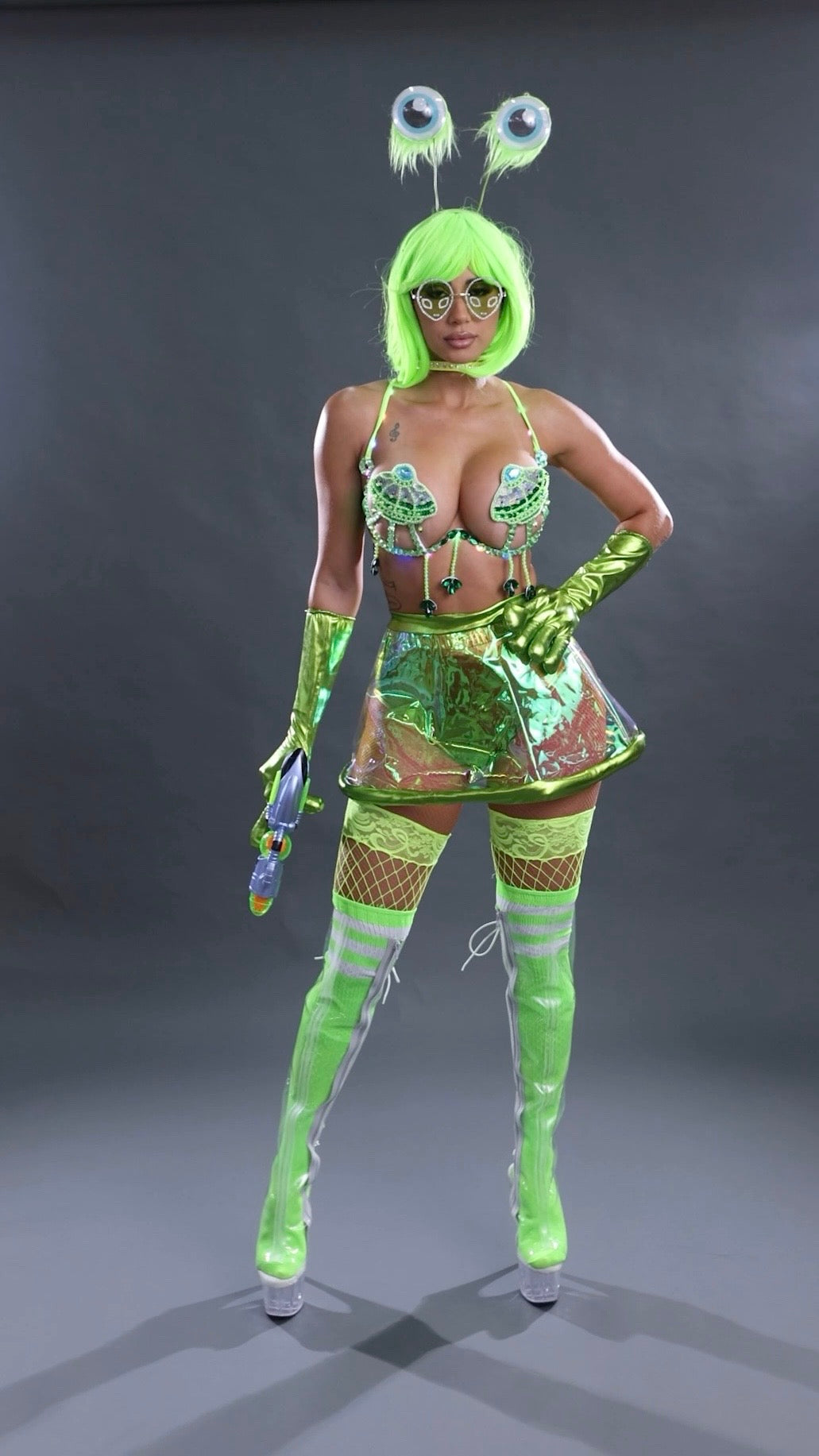 Person wearing a green alien costume with a hood and gloves on a gray background